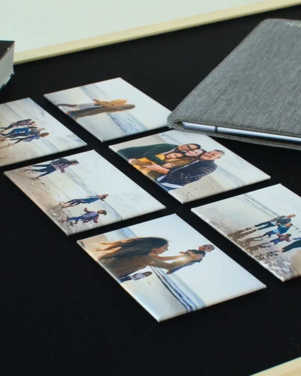 Sześć personalizowanych foto magnesów z rodzinnymi zdjęciami ułożonych na czarnej powierzchni obok notesu, rysika i książki – elegancka dekoracja oraz praktyczny pomysł na prezent.